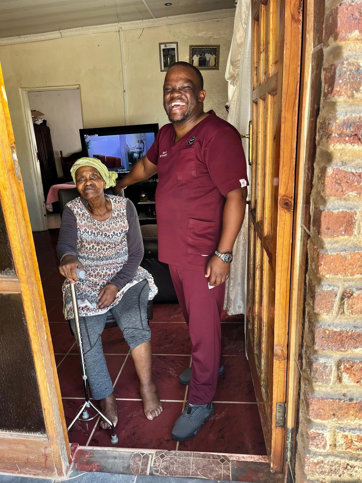 Woman sitting with a cane and a smiling man standing in doorway of a home.